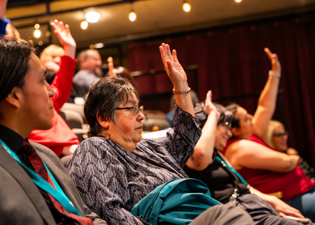Participant Engagement at an Arts BC Event A participant with a raised hand engages in discussion at an Arts BC event, seated among others in a lively, collaborative setting.